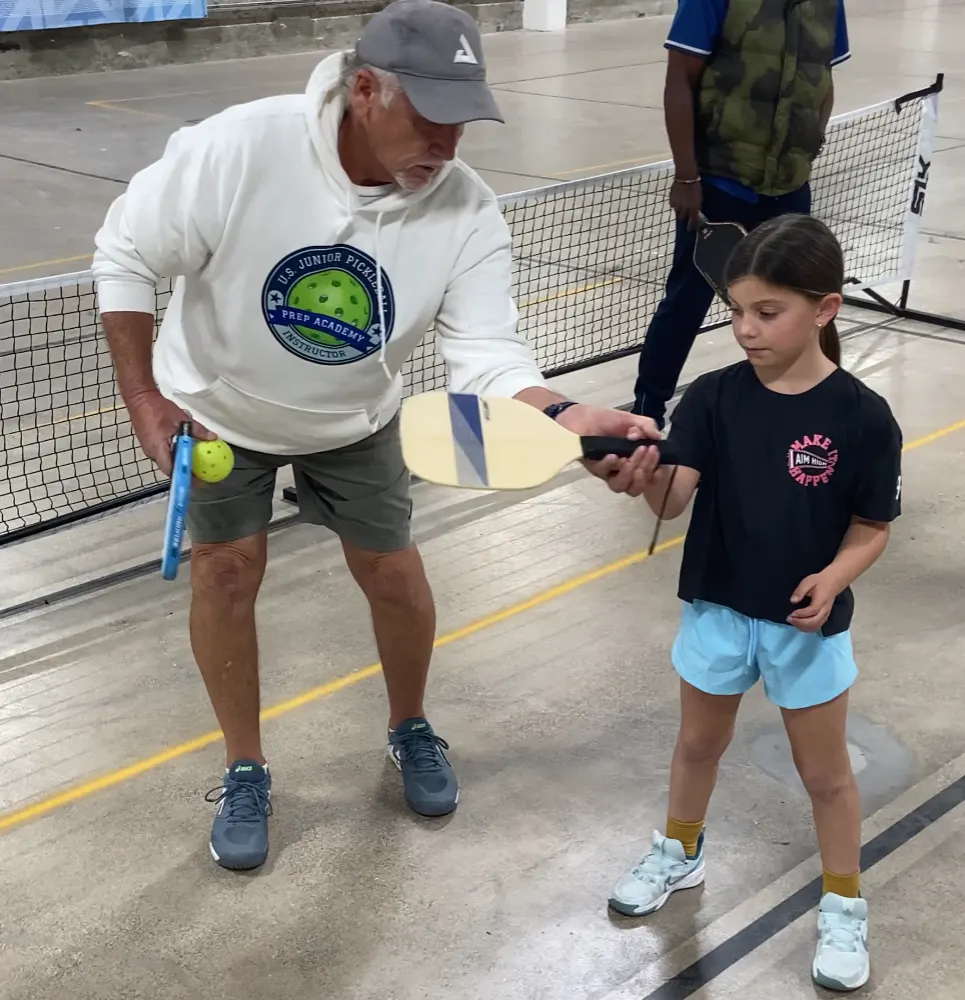 pickleball coach teaching yuoung pickleballs player how to hold the raquet